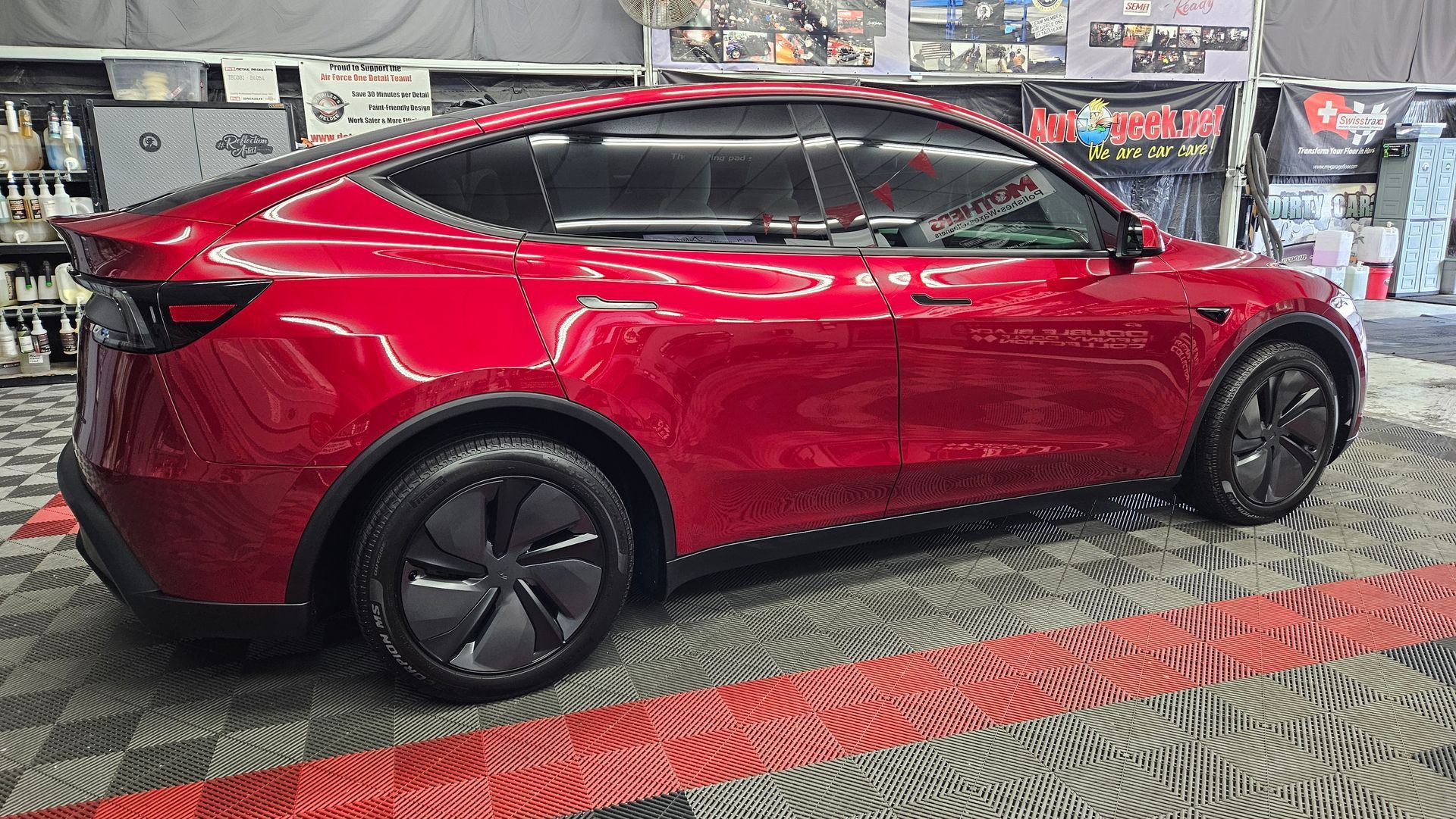 Red Tesla Model Y parked indoors on a showroom floor, side view