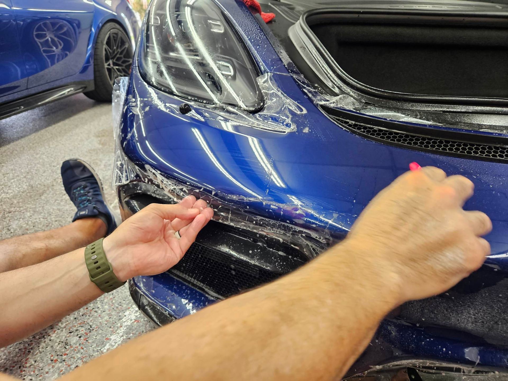 A person is applying a protective film to the front of a blue car.