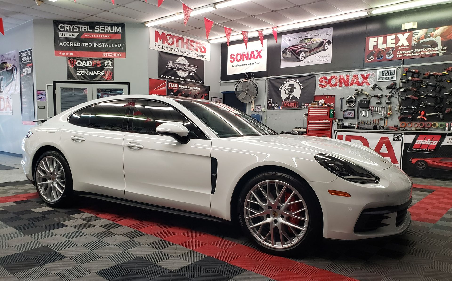 White Porsche Panamera on display inside a detailing shop with product advertisements.