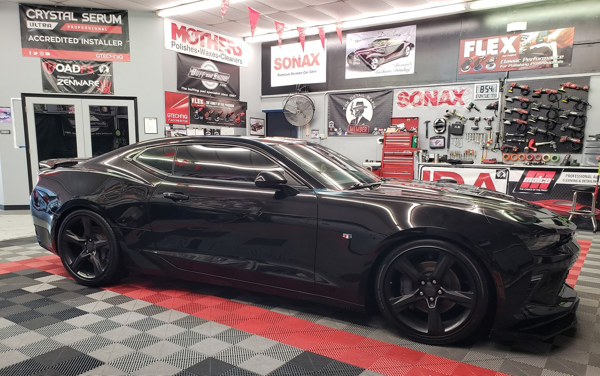 Black sports car in a shop with product displays and flags.