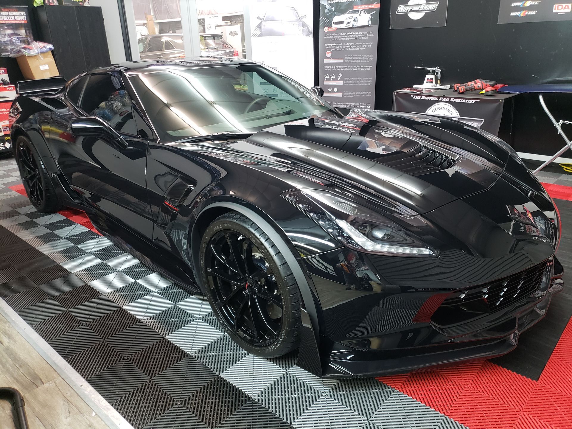A black corvette is parked in a garage on a checkered floor.