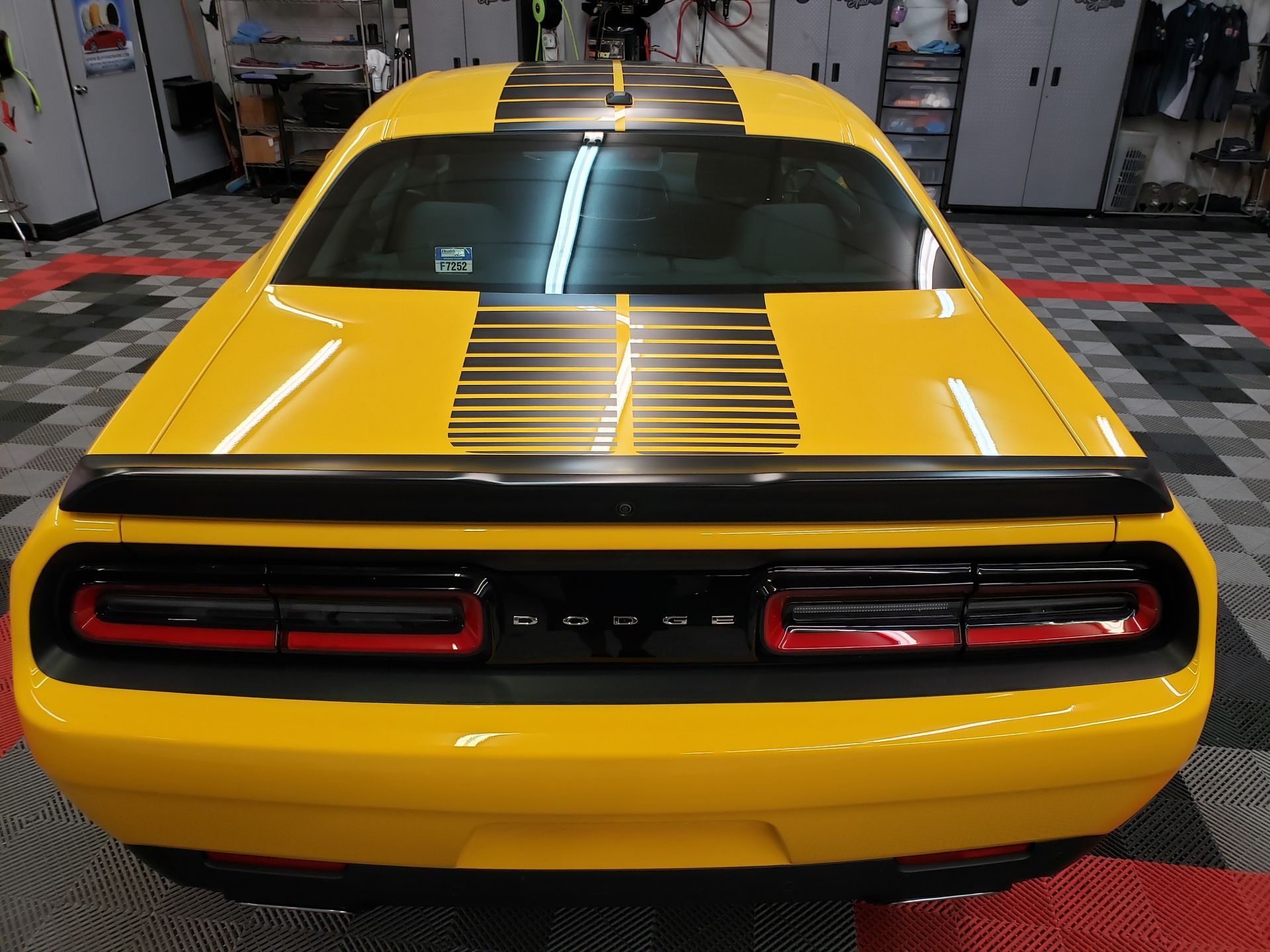 A yellow dodge challenger with black stripes is parked in a garage.