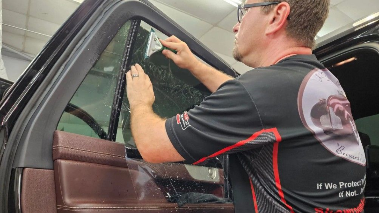 Man applying window tint to a car window in a garage.