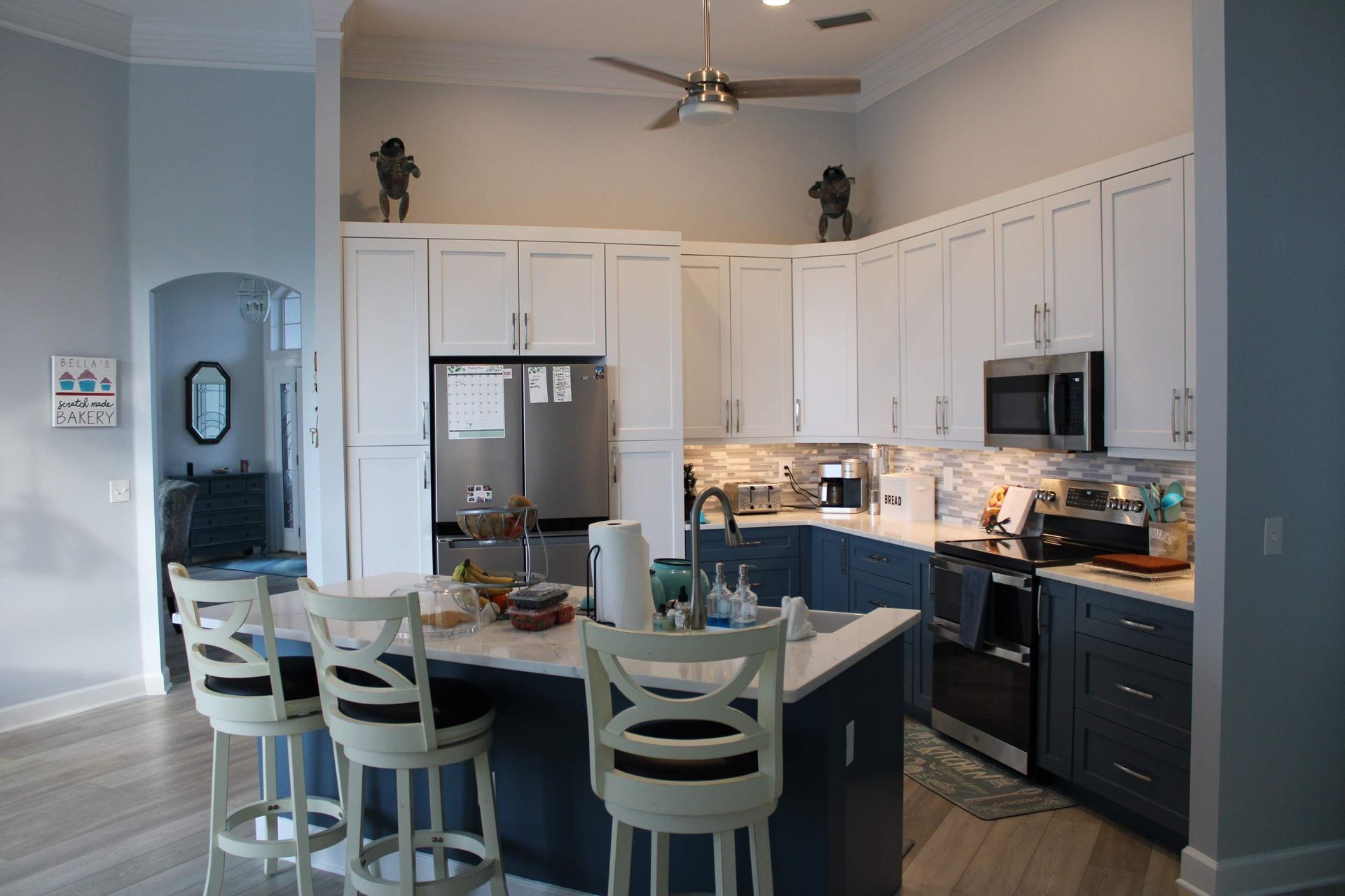 A kitchen with blue cabinets and white stools and a ceiling fan.