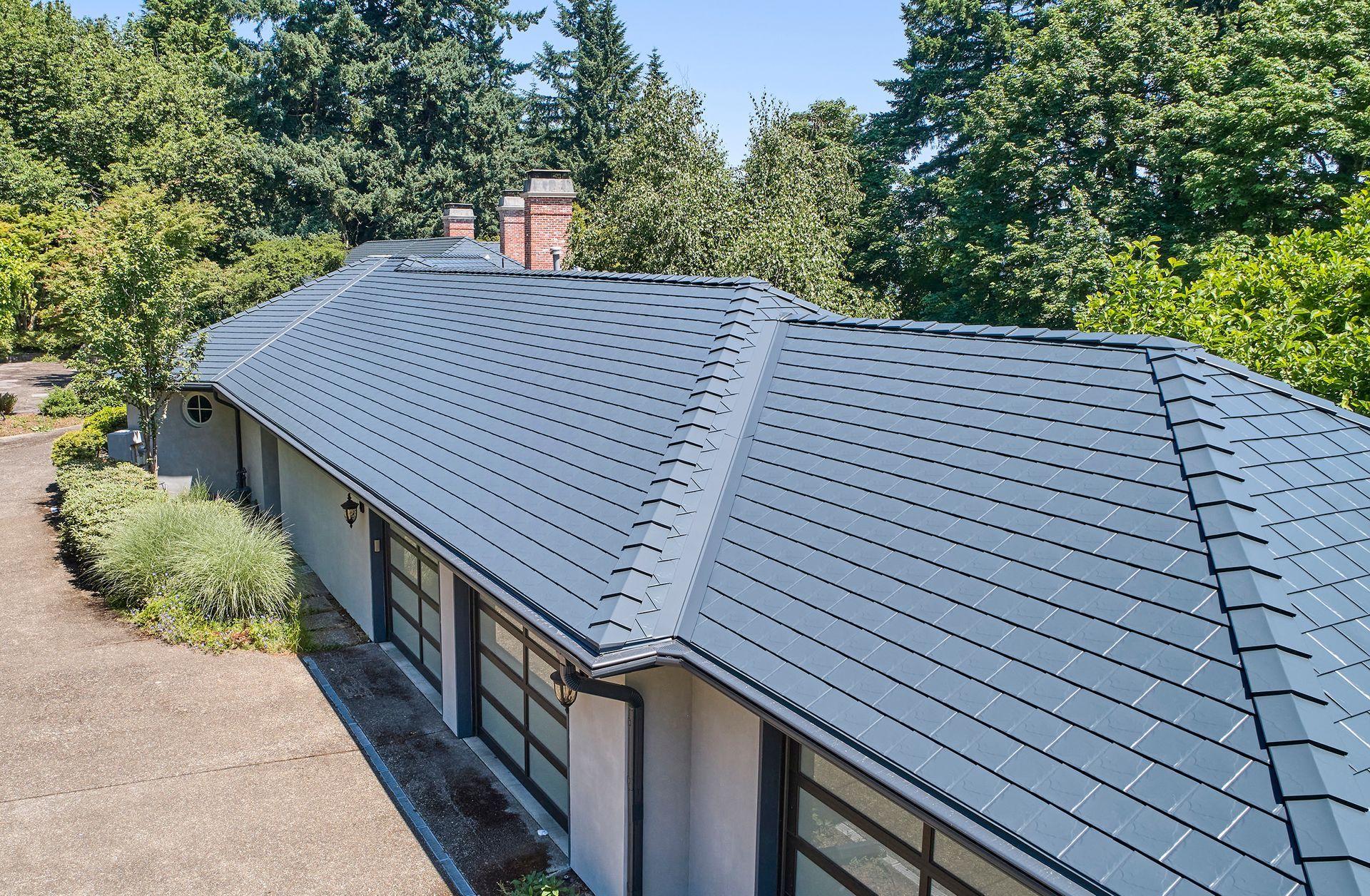 Rear view of a multi-level home in Dunthorpe with a Deep Charcoal Interlock aluminum slate roof. Installed by Interlock Metal Roofing, the system integrates beautifully with rounded balconies, metal turret roofing, and large windows that overlook the backyard garden.