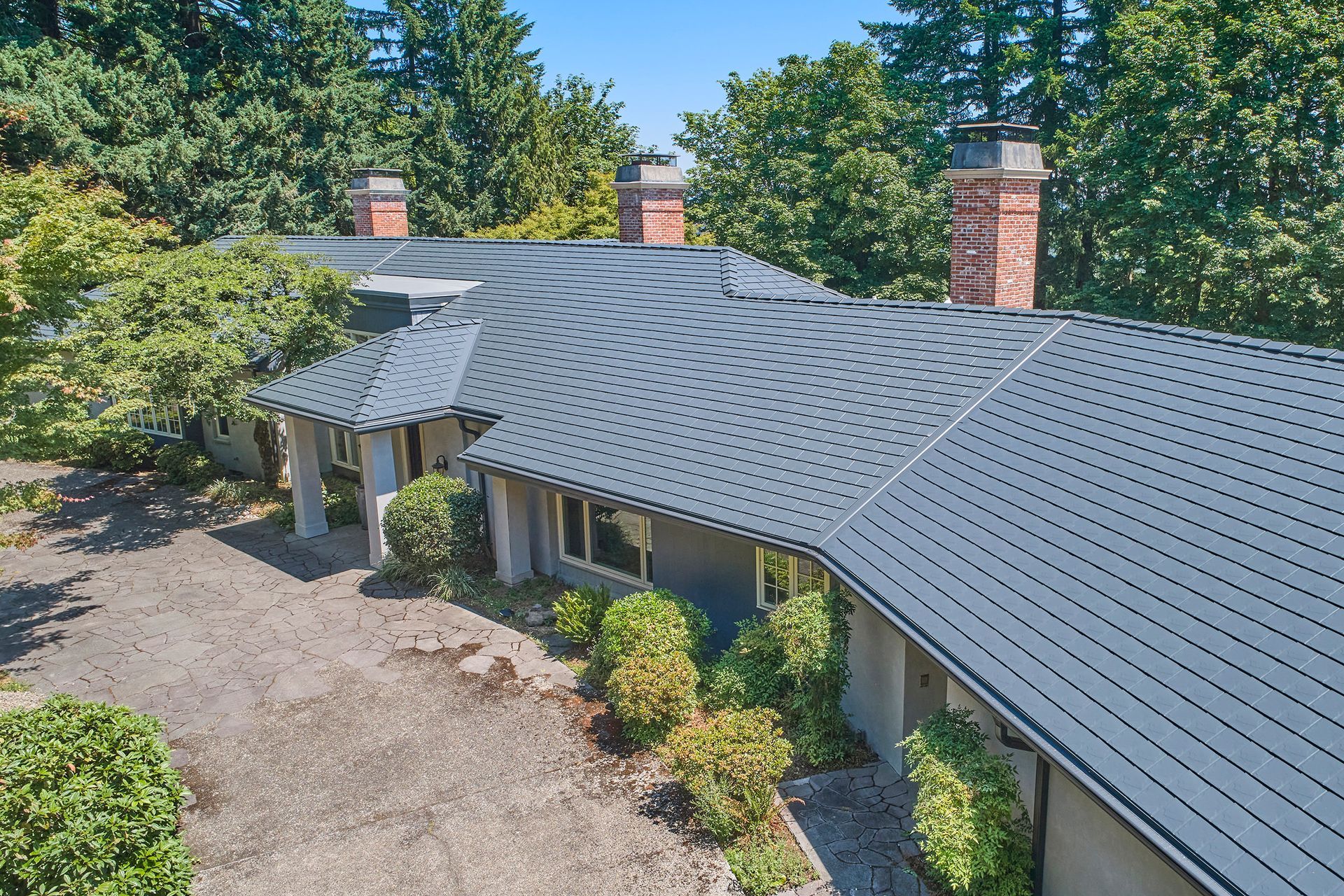 Elegant front-facing perspective of a Dunthorpe estate in Portland OR with a deep charcoal Interlock Metal Roofing aluminum slate roof. The home showcases clean lines and lush landscaping, paired with lifetime metal roof protection.