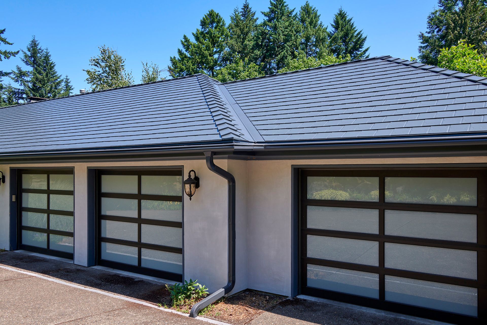 Artistic close-up through tree leaves capturing the deep texture and interlocking seams of an Interlock Slate roof in Dunthorpe. The charcoal metal shingles provide eco-conscious homeowners with long-term peace of mind and visual sophistication.