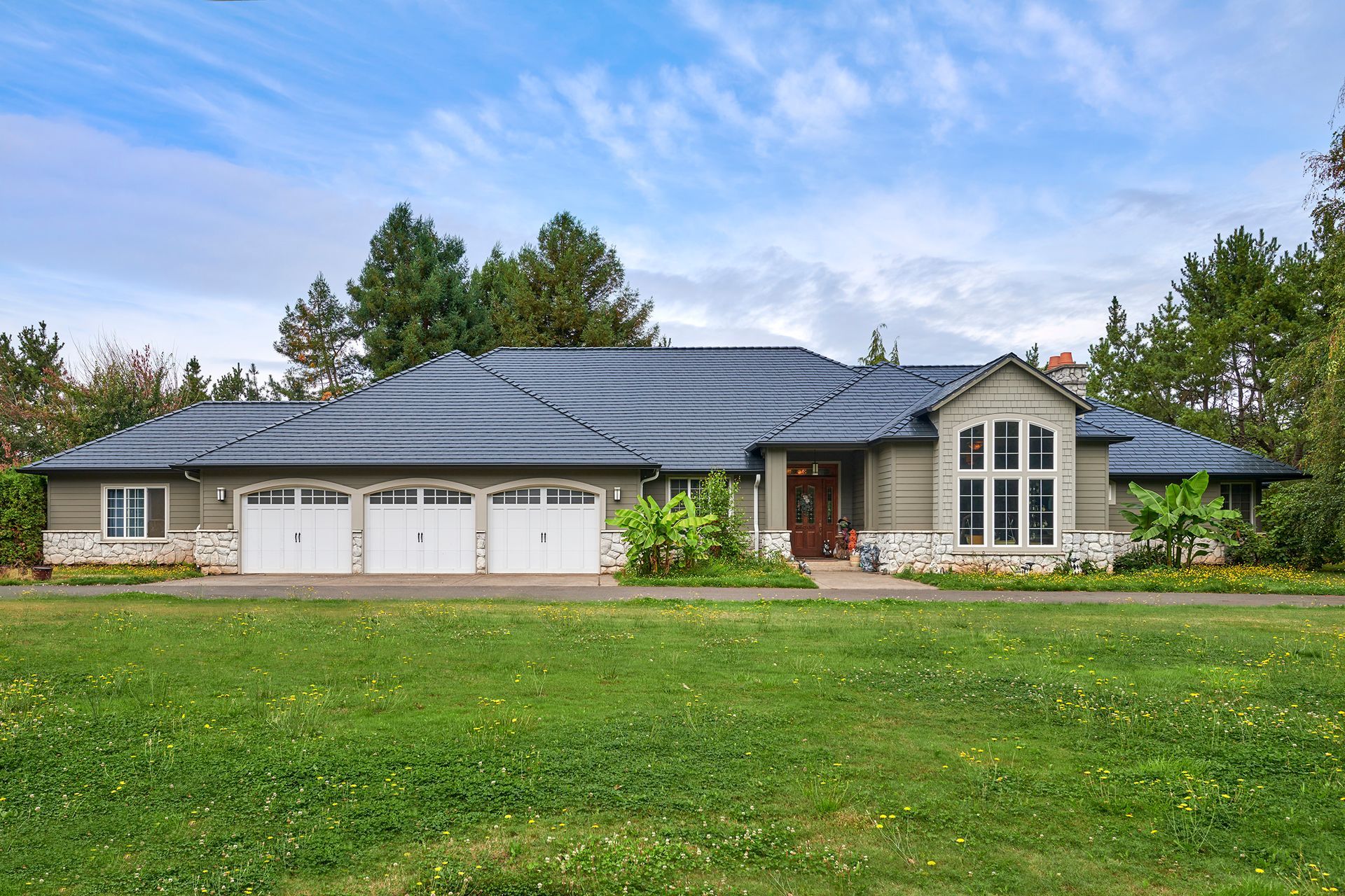 Front-facing view of a modern single-level home in Ridgefield, WA, featuring a Deep Charcoal Interlock Slate aluminum roof installed by Interlock Metal Roofing. The heavy-gauge aluminum roof complements the home’s stone accents and triple-car garage while offering long-term durability, fire resistance, and enhanced curb appeal in Clark County.