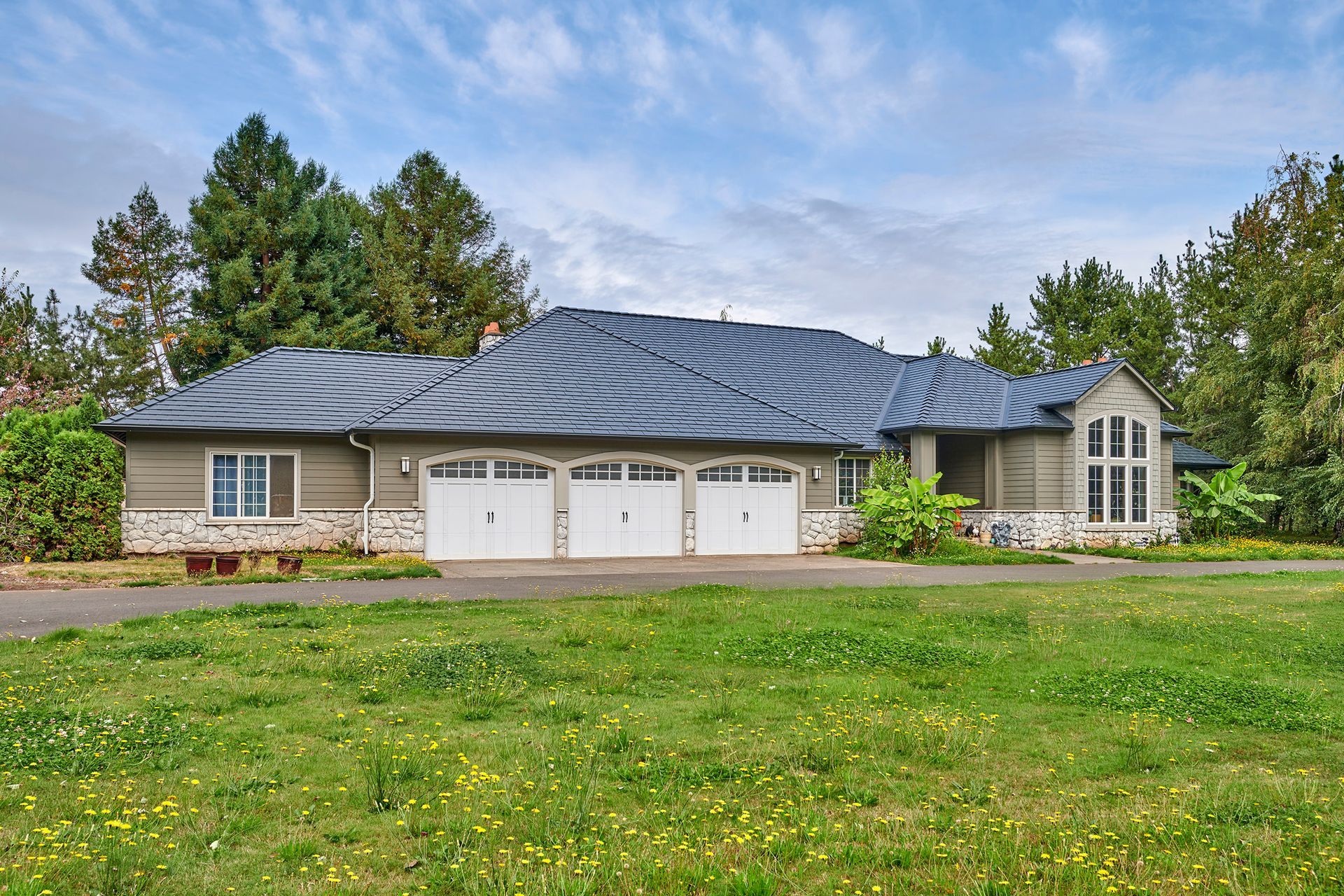 Wide-angle shot of a Deep Charcoal aluminum slate roof installed by Interlock Metal Roofing on a craftsman-style home in Ridgefield, WA. Surrounded by forested landscaping, this home benefits from a lifetime metal roofing system designed for long-term weather resistance and low maintenance.
