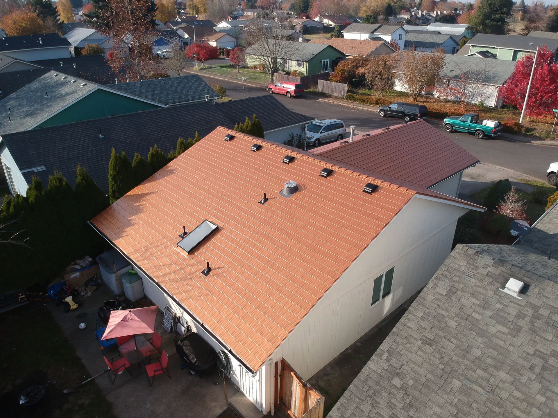 Elevated corner view of a single-story home in the Southeast Mill Creek neighborhood of Salem, OR, featuring a bold Copper Penny Interlock Cedar Shingle Roof made from heavy gauge aluminum, installed by Interlock Metal Roofing. The architectural-grade metal shingles authentically replicate real cedar shake with the color of new copper—delivering unmatched style without the patina. Key rooftop details include a solar tube skylight, strategically placed black vent caps, and a fully sealed pipe vent—all integrated with the four-way interlocking system to resist wind uplift and moisture infiltration. The roof’s coppery hue beautifully contrasts with the rustic, weathered wood siding and oversized white-trimmed windows, while surrounding native shrubs and trees create a picturesque Oregon landscape backdrop. Ideal for homeowners seeking a classic copper aesthetic with the strength and performance of aluminum.