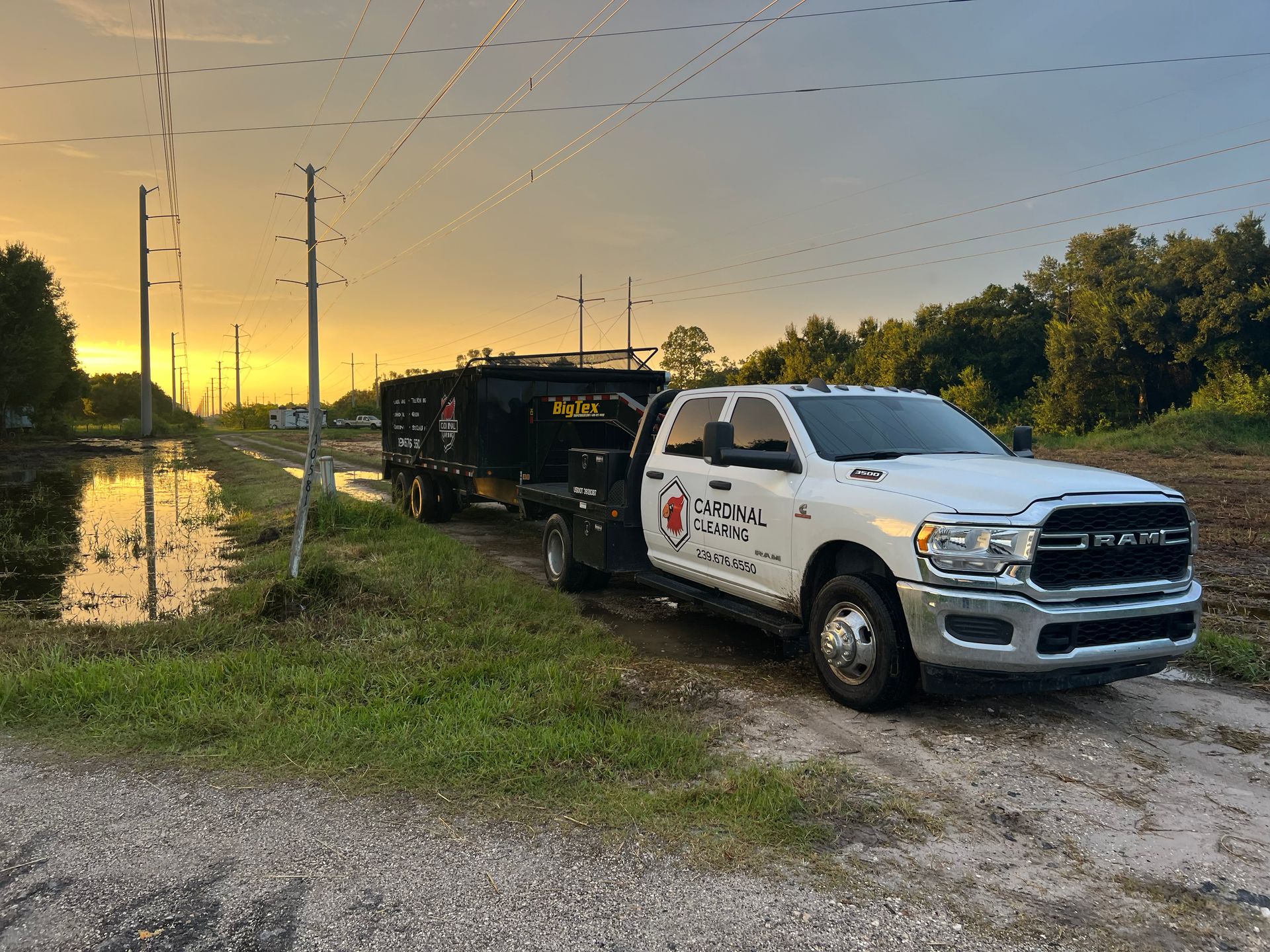 White truck with trailer parked on dirt road near flooded area at sunset.