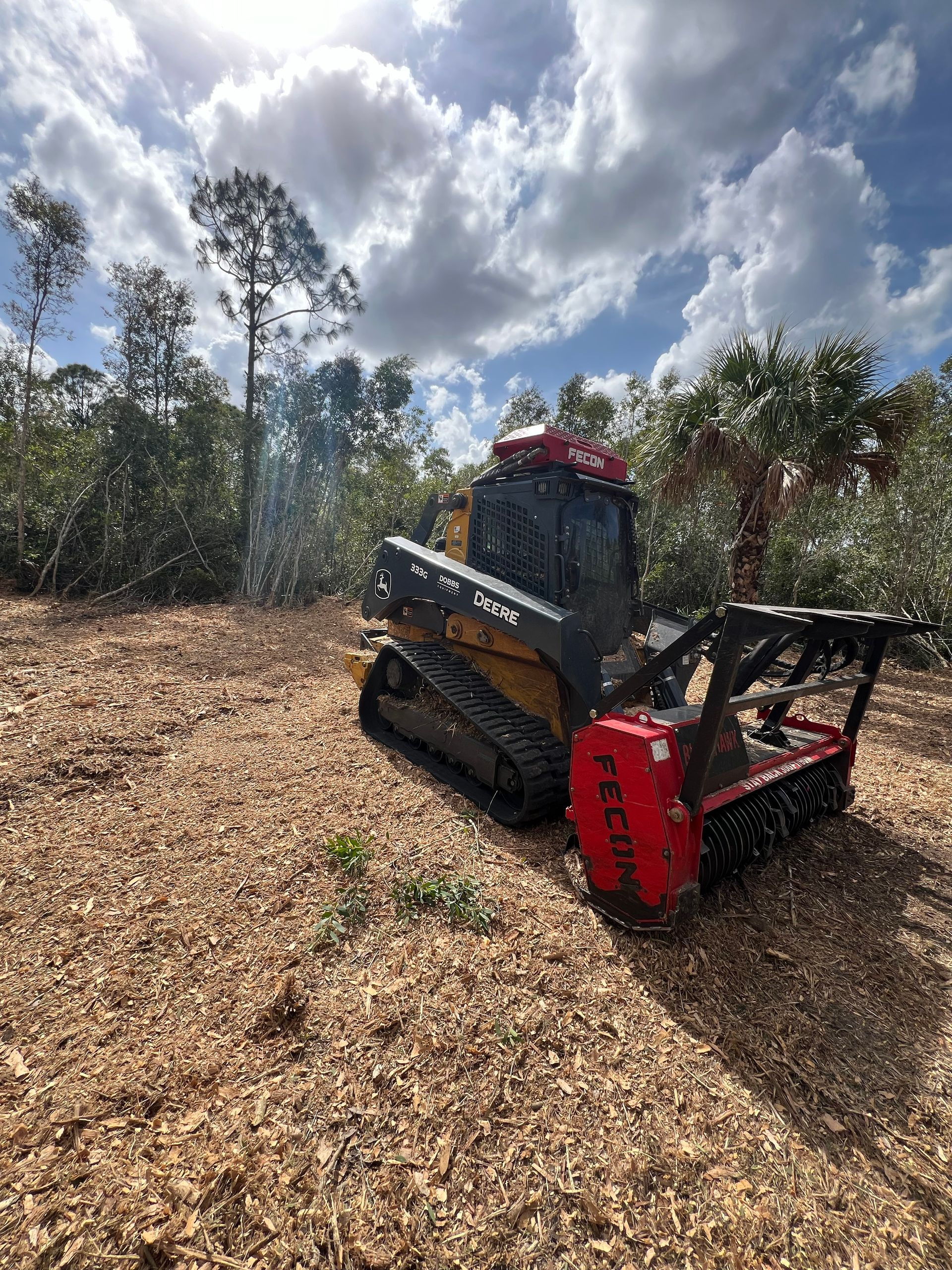 A mulching machine working in a wooded area, creating wood chips under a cloudy sky.
