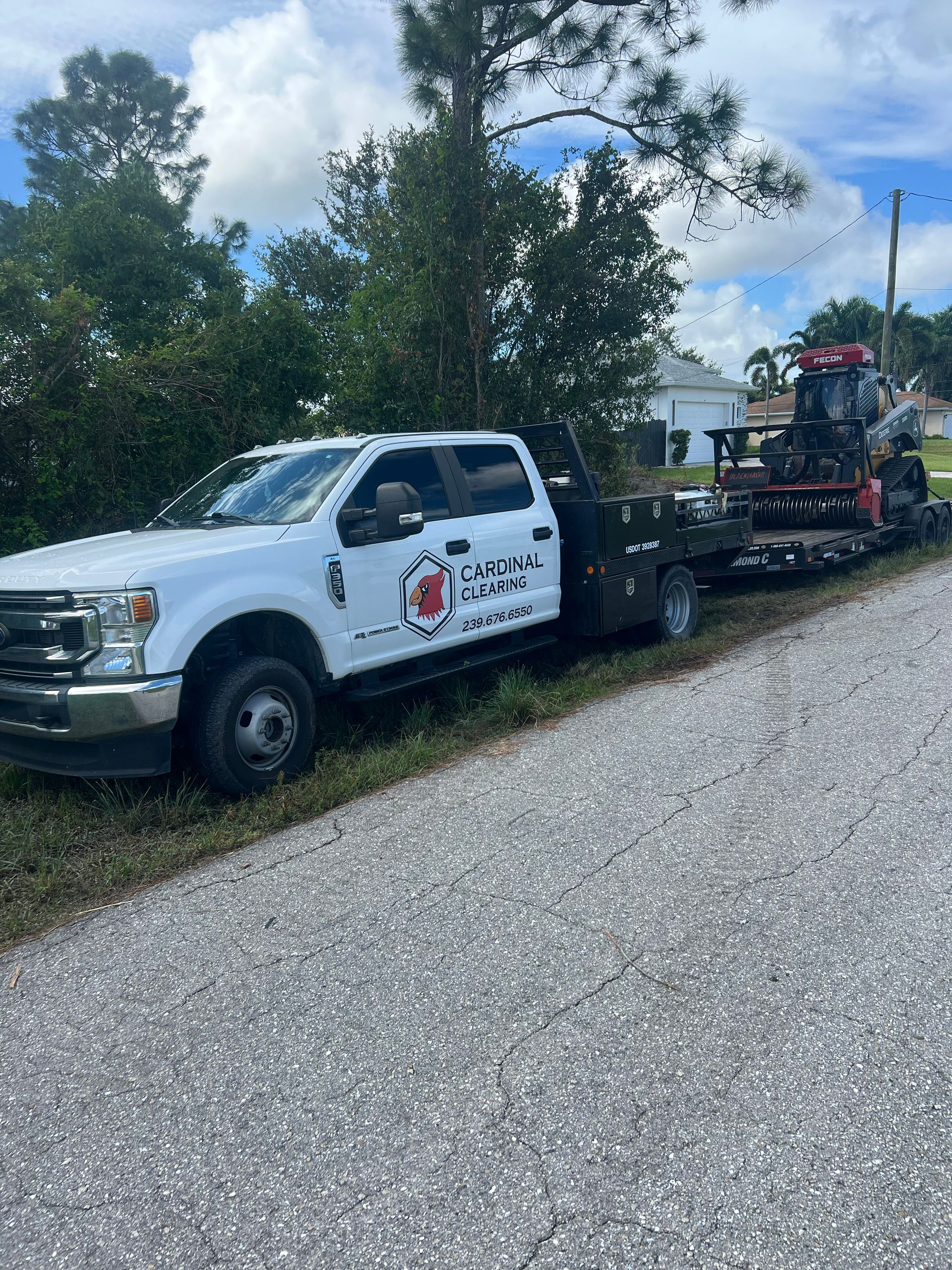 White pickup truck with a flatbed trailer hauling a tractor on a paved road.