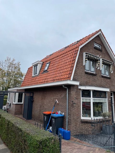 Een bakstenen huis met een rood pannendak en veel ramen.