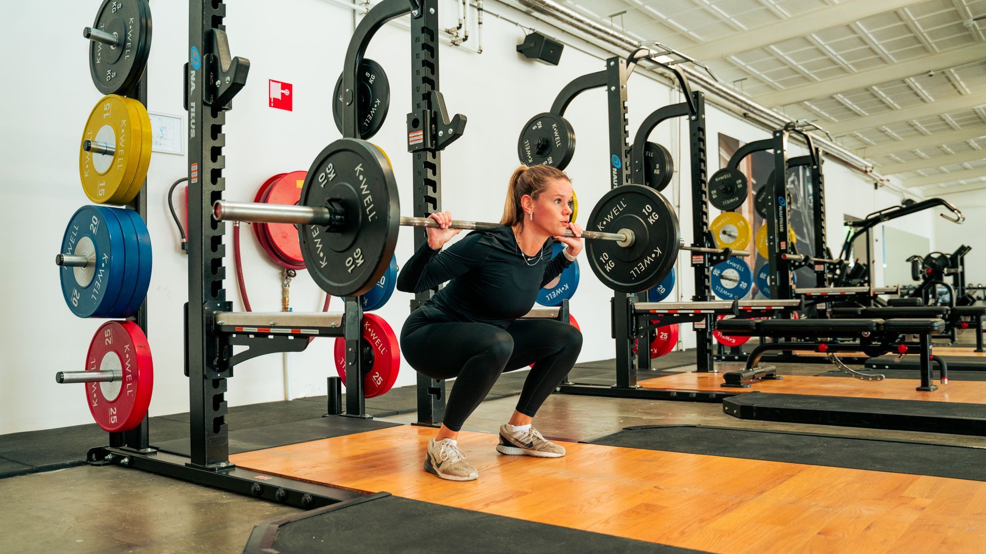 Een vrouw doet een squat met een halterstang in een sportschool.