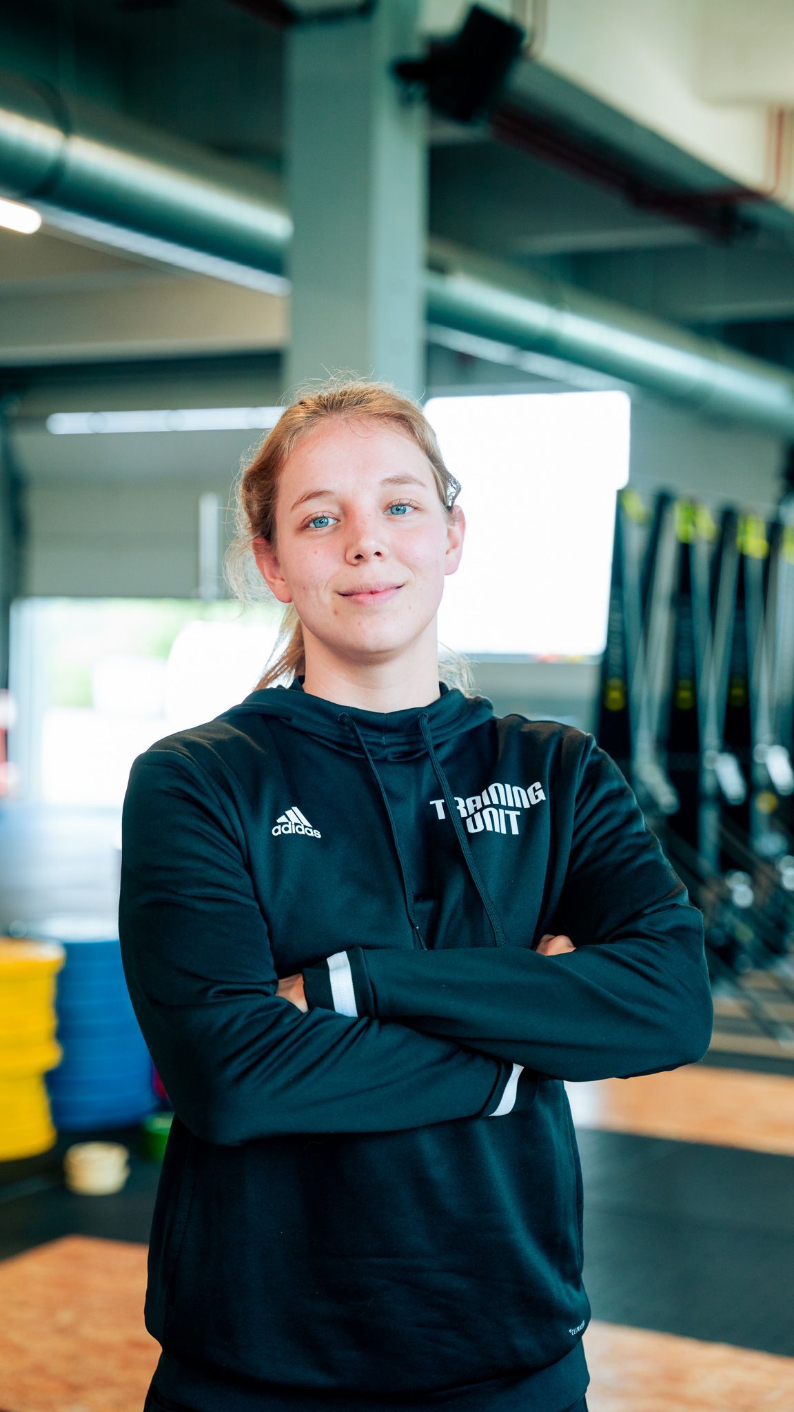 Een jonge vrouw staat met haar armen over elkaar in een sportschool.