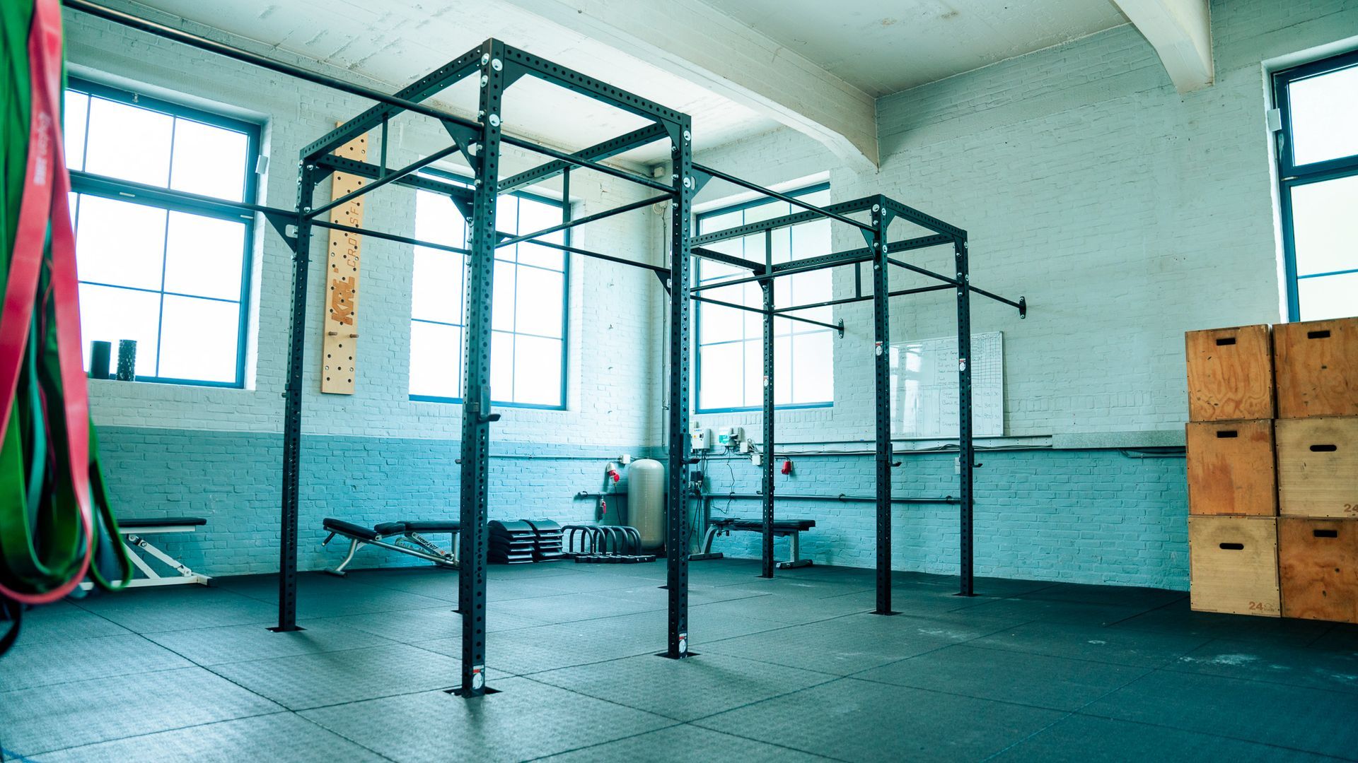 Lege sportschool met metalen pull-up rekken, hangende straps en gestapelde houten boxen bij blauwe r