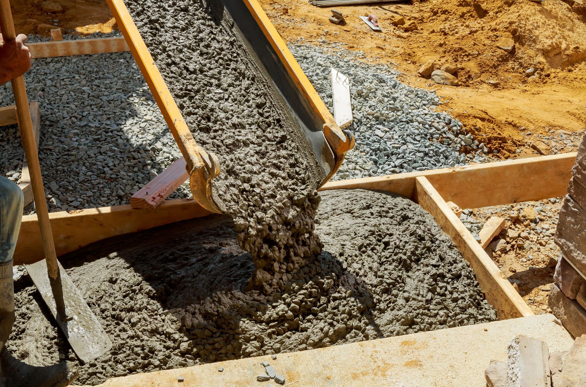 A person is pouring concrete into a hole with a shovel.