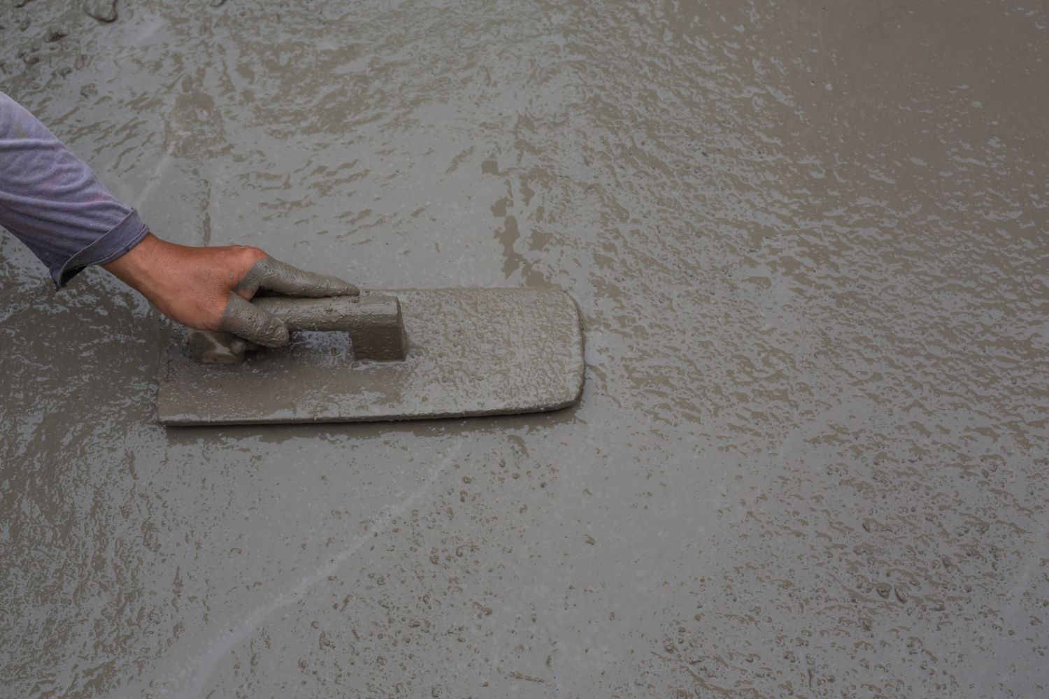 A person is using a trowel to level a concrete floor.