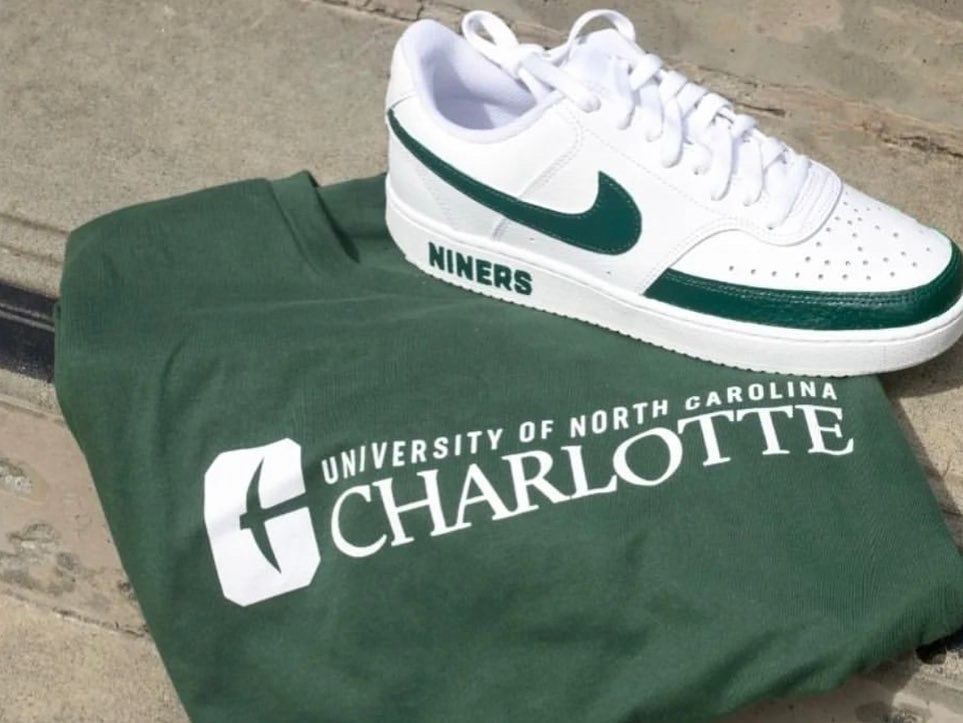 White and green Nike shoe and green UNC Charlotte t-shirt on a concrete surface.