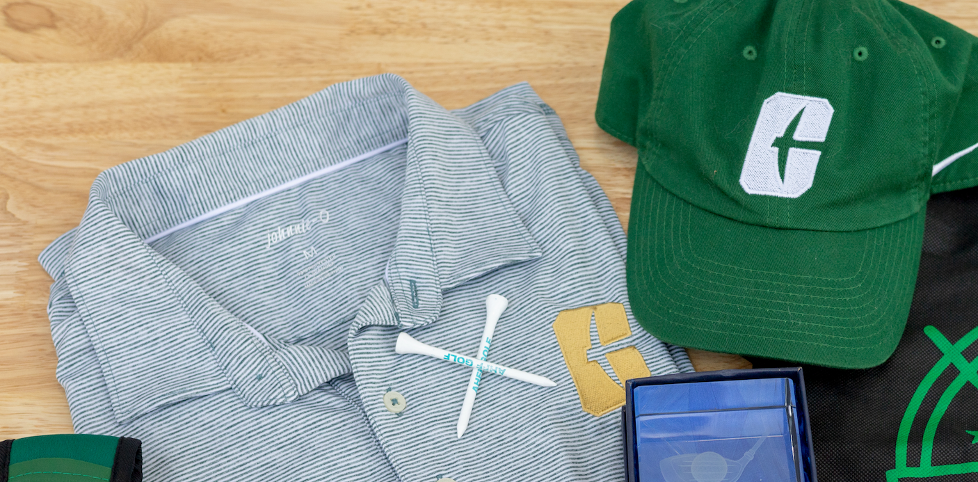 Golf shirt, hat, and accessories on a wooden surface. The shirt is grey with white stripes, the hat is green with a 