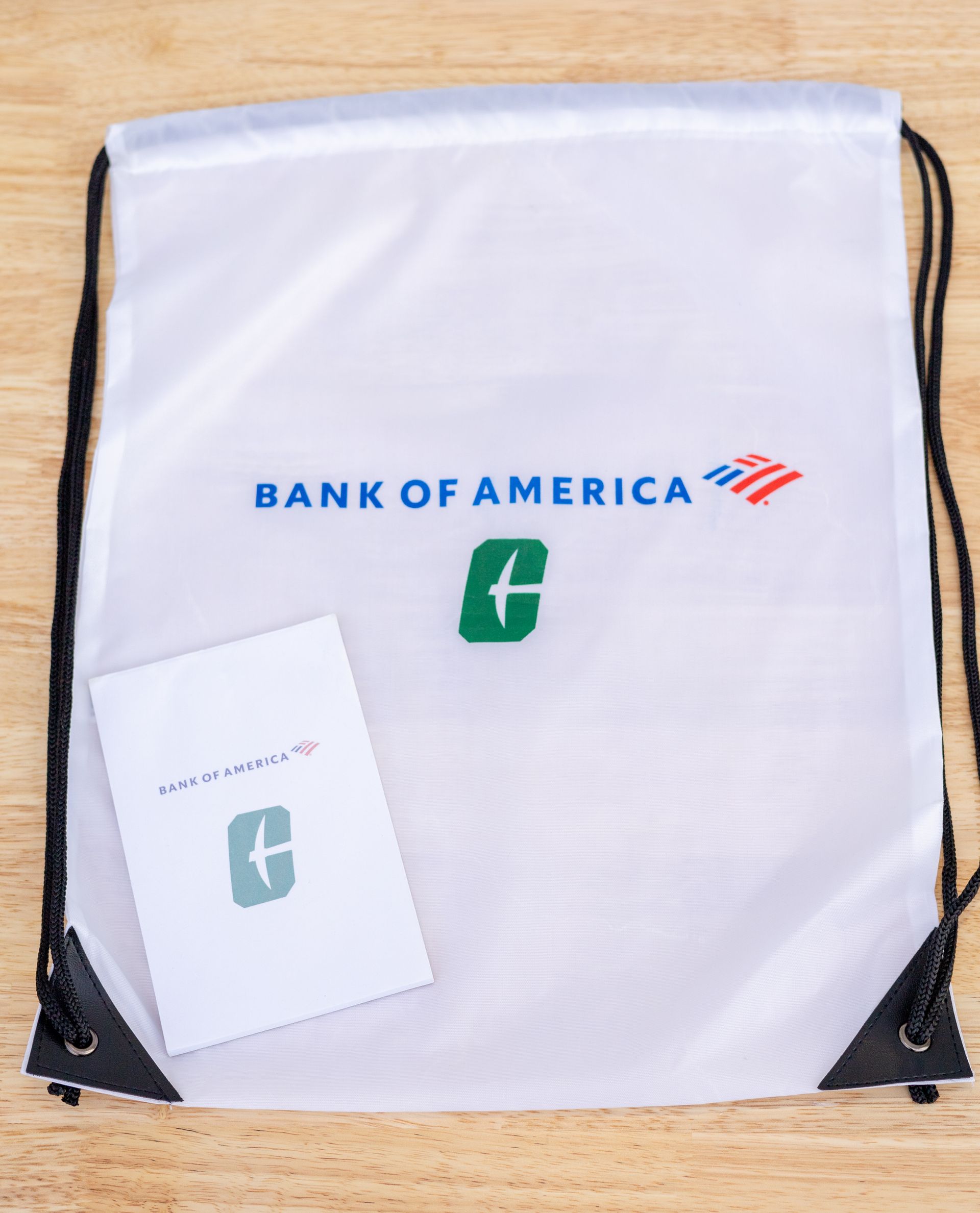 White Bank of America drawstring bag with logo and a small card on a wooden surface.