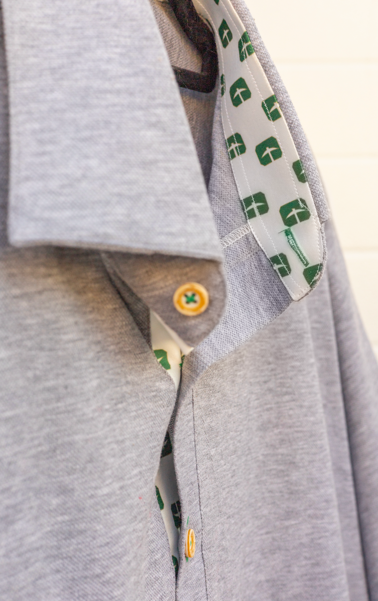 Close-up of a gray shirt collar with a gold button and patterned lining.