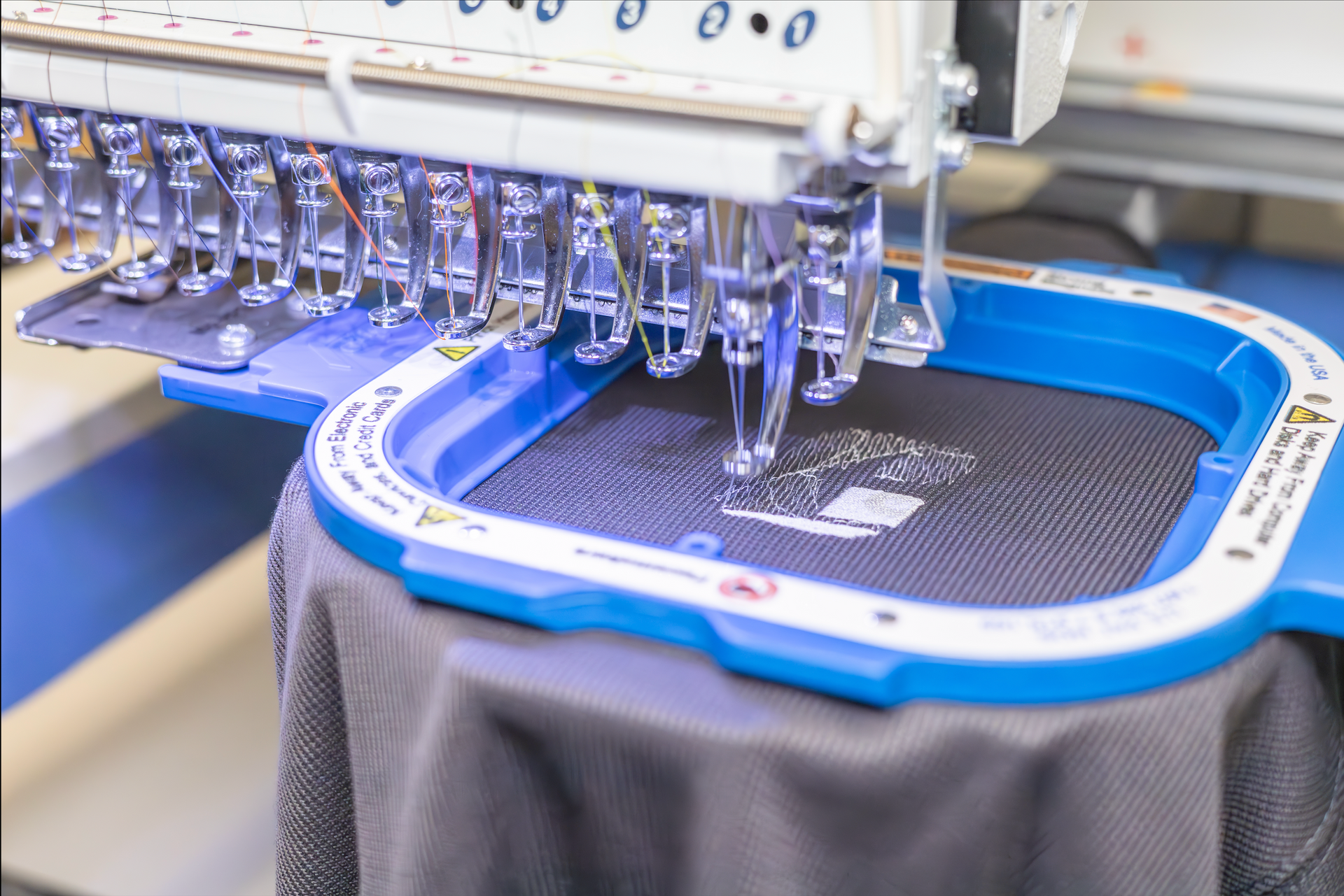 Embroidery machine stitching design onto dark gray fabric held in a blue hoop.