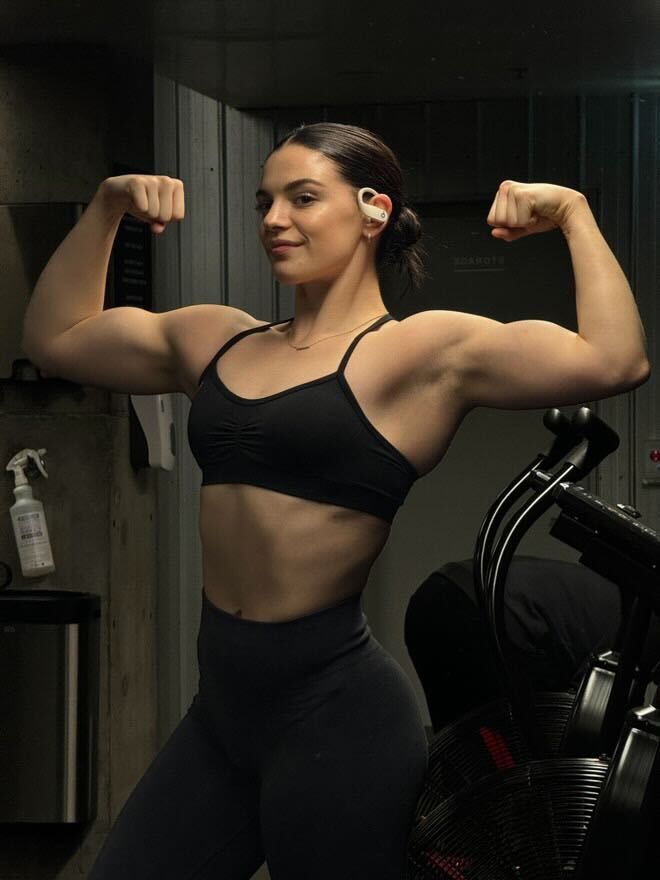 A woman is flexing her muscles in front of a mirror in a gym.
