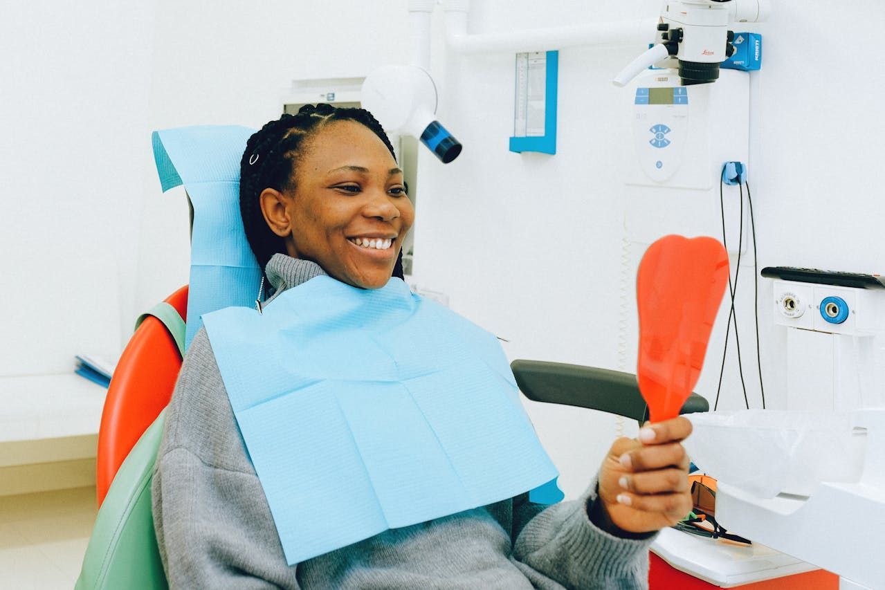 a woman is sitting in a dental chair looking at her teeth in a mirror.
