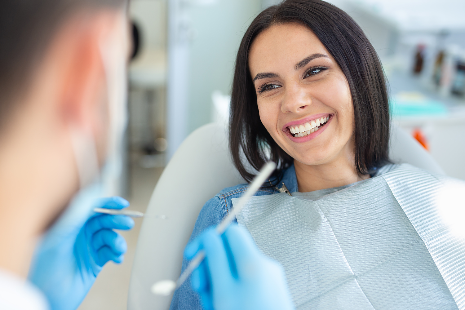 girl sitting in dental chair smiling showing her teeth while the dental assistant looks at her teeth