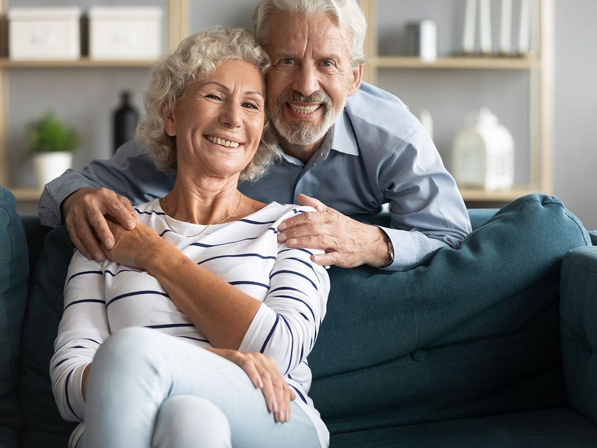 older couple leaning in together to smile at the camera and showing off their dentures