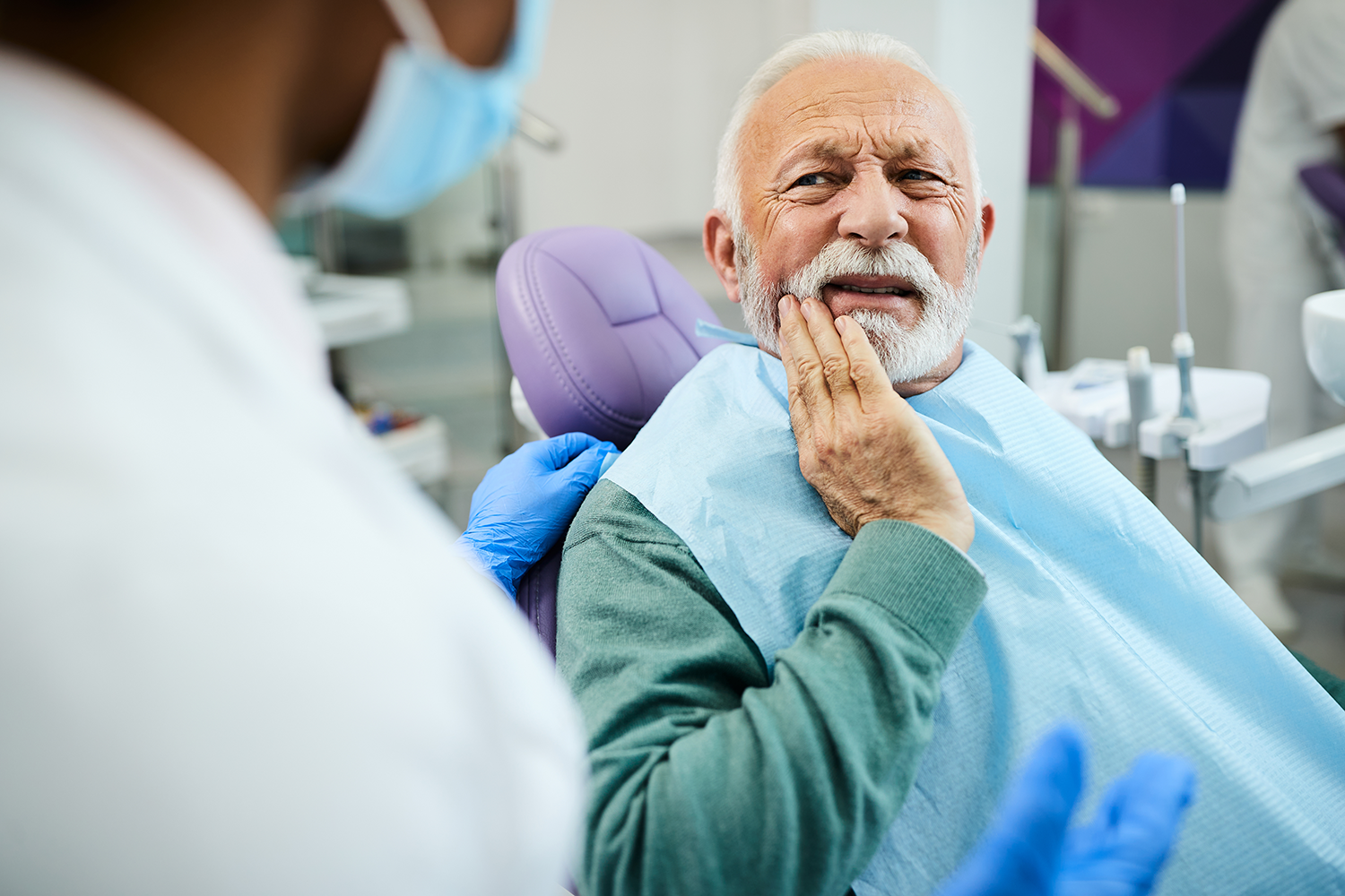 guy sitting in dental chair in pain holding hand up to his mouth