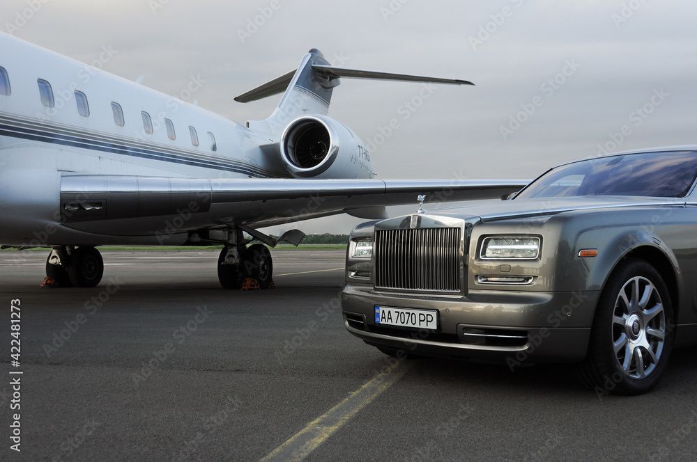 Silver Rolls Royce parked next to a private jet on an airfield.