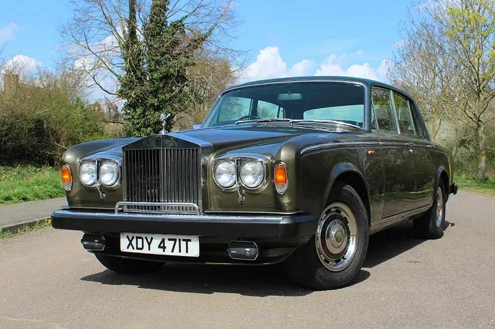 Green vintage Rolls Royce parked on a road, sunny day.