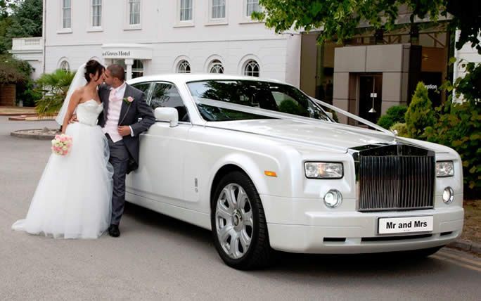 Bride and groom kissing next to a white Rolls Royce at a wedding.