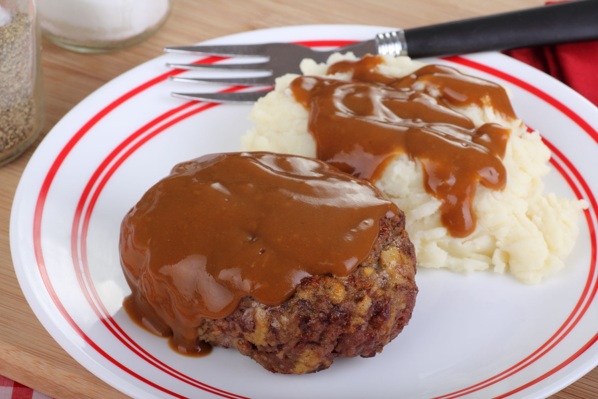 A white plate topped with meat and mashed potatoes with gravy and a fork.