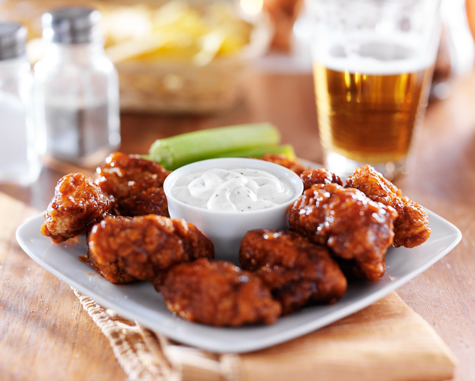 A plate of chicken wings with ranch dressing and celery next to a glass of beer.