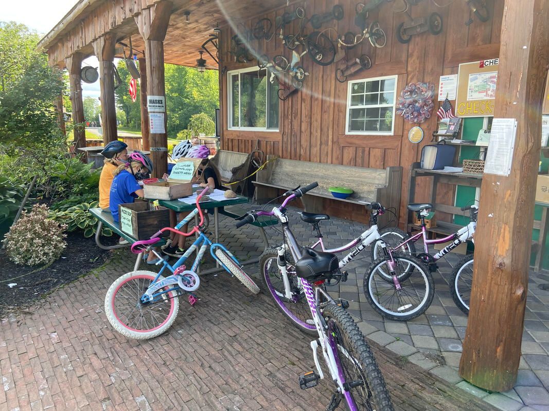 A group of people are sitting at a picnic table with bicycles parked in front of a wooden building.