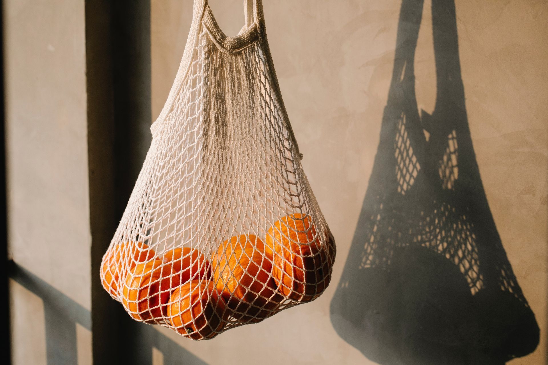 A string bag filled with oranges is hanging on a railing.
