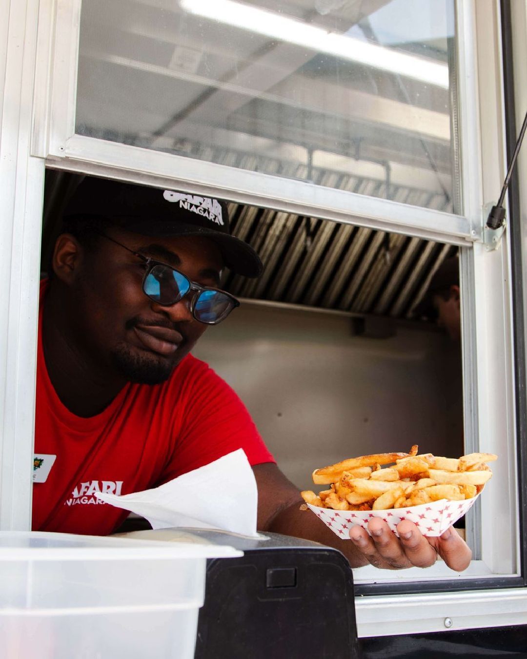 a man holding a bowl of french fries wearing a red safari niagara shirt at a food truck in safari niagara ontario