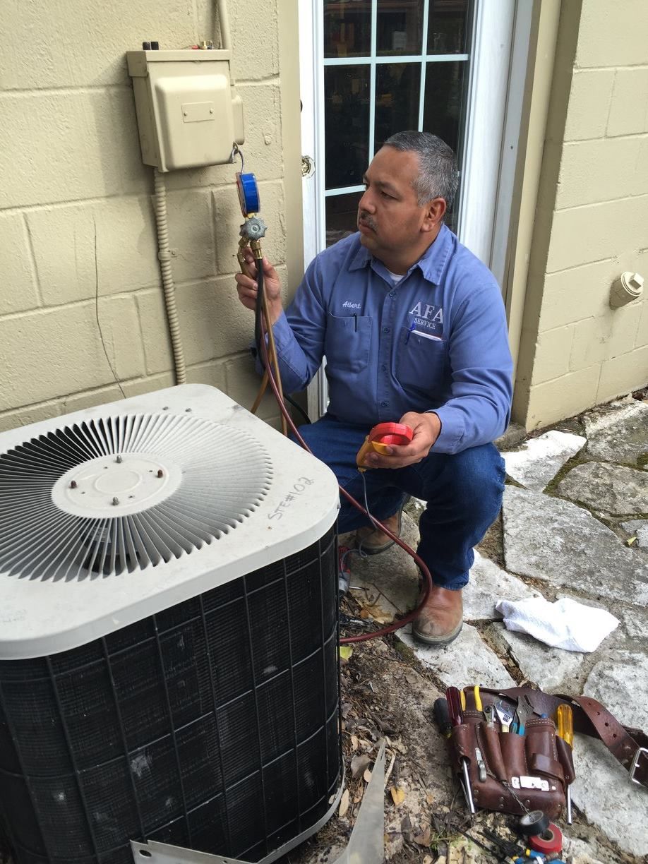 A man is kneeling down next to an air conditioner from AFA Service