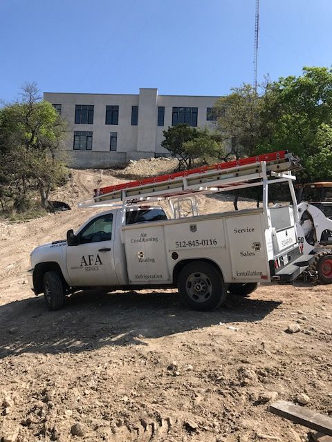A white truck with a ladder on top of it is parked in a dirt field from AFA Service
