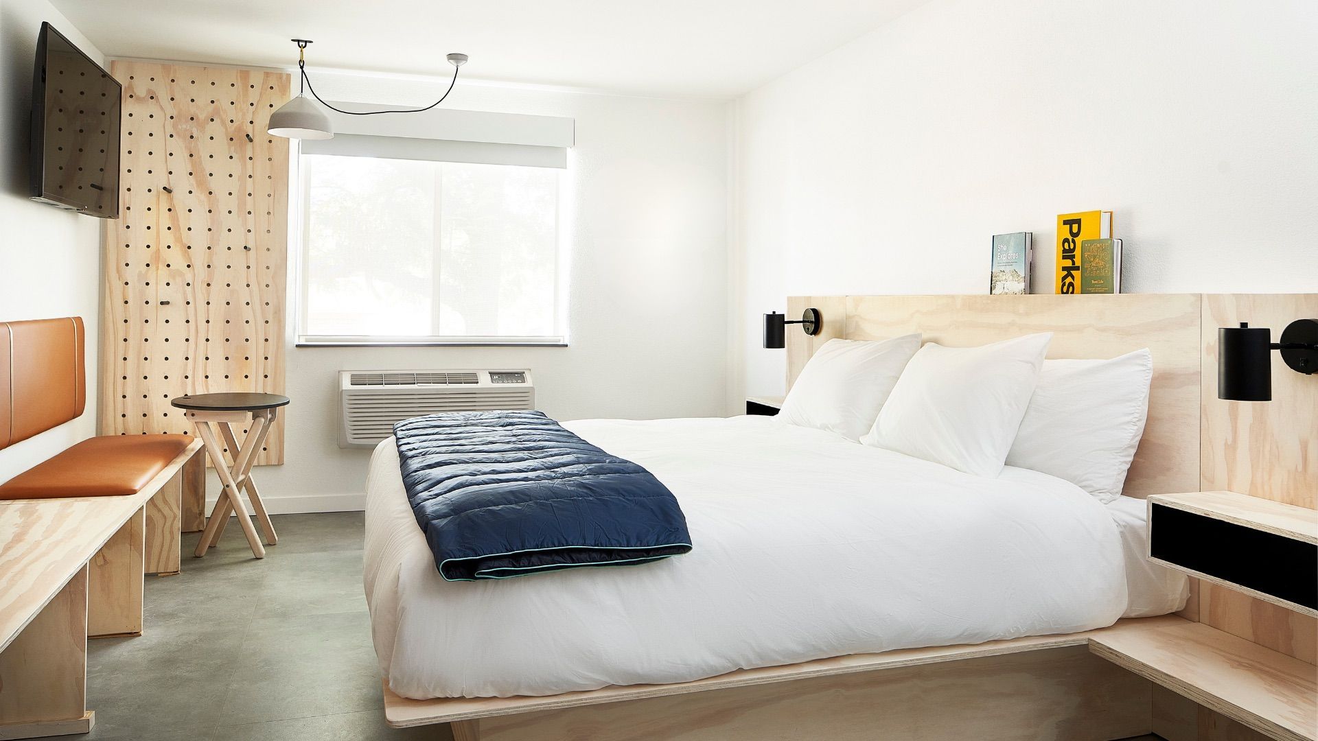 Modern hotel room with a bed, desk, and pegboard wall. Bright and minimalist.