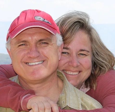 Couple embracing, smiling; man in red cap, woman with blonde hair, outdoors.