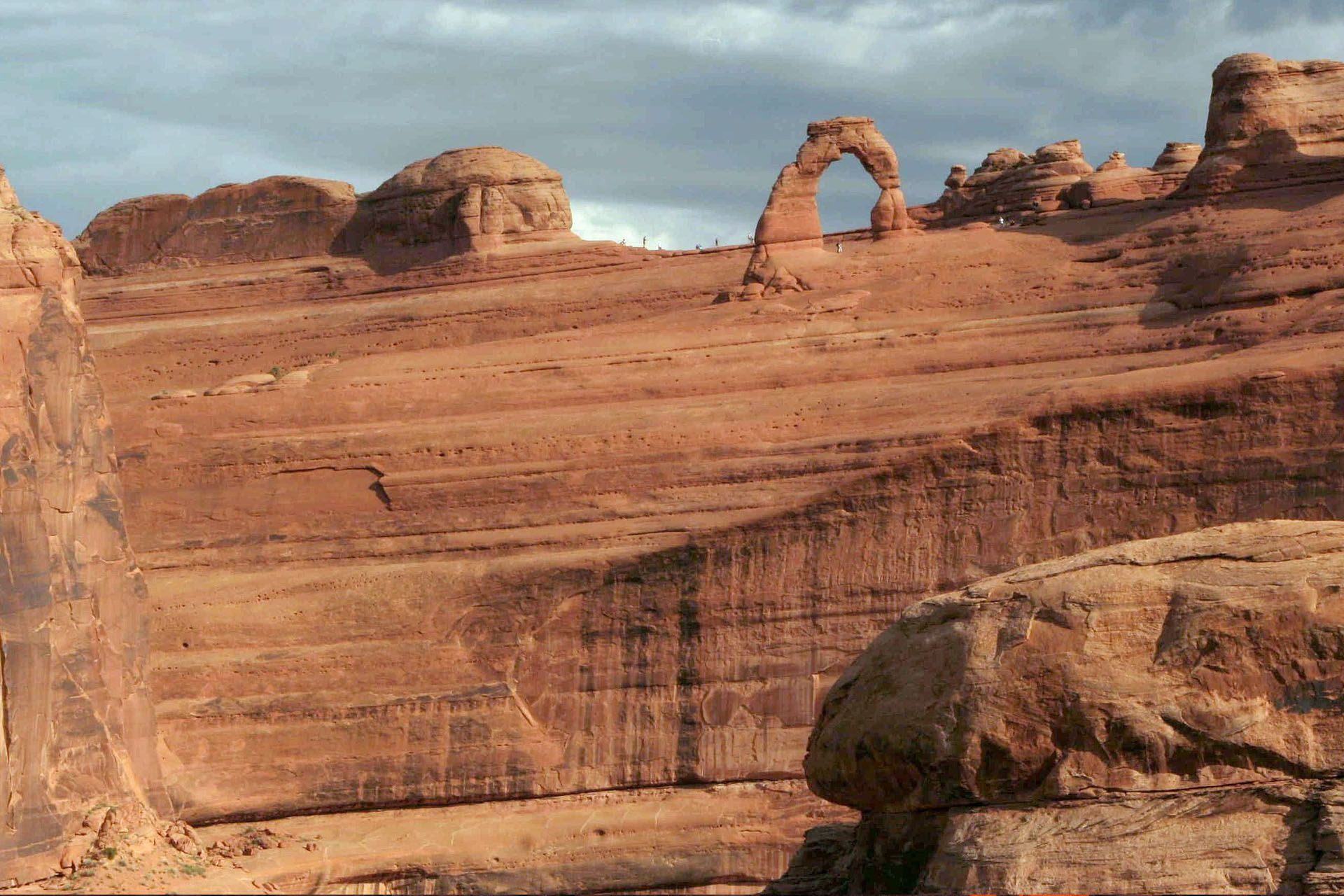 Arches National Park landscape featuring Delicate Arch in the distance; red rock formations under cloudy sky.