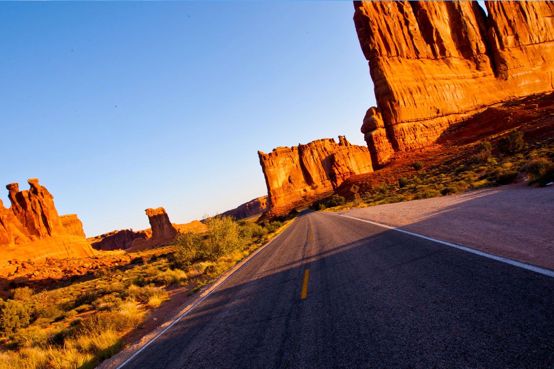 Road winding through red rock formations under a clear blue sky.
