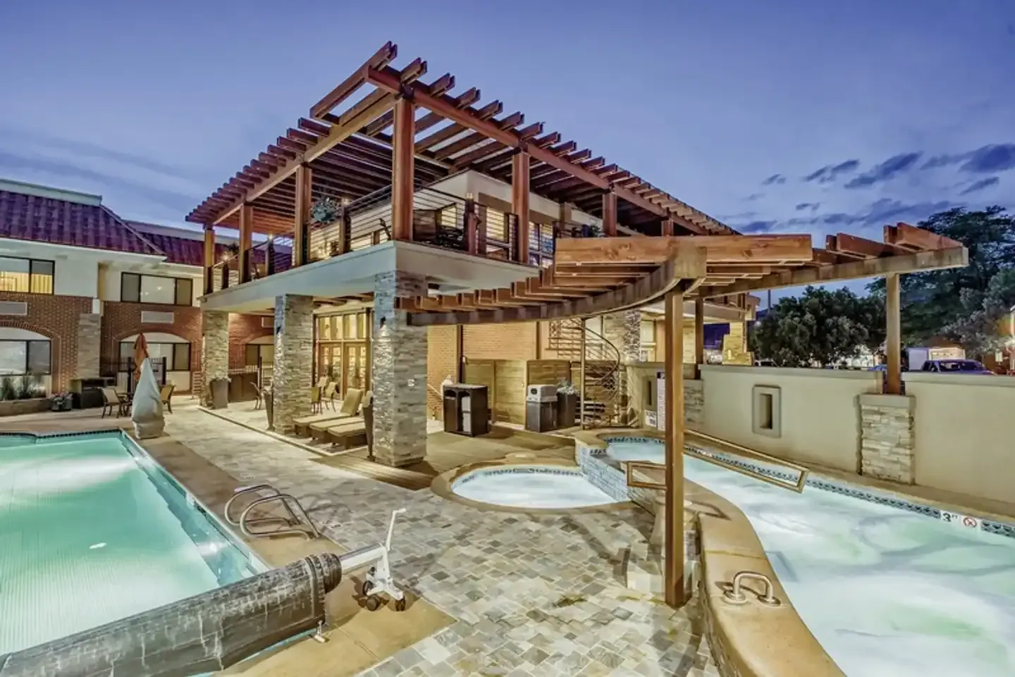 Swimming pool area with pergola and building, night.