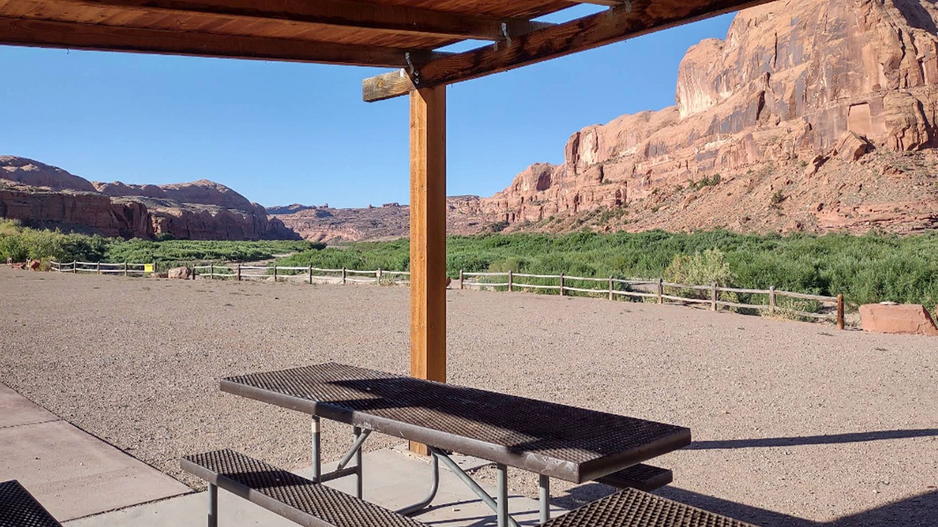Covered picnic table area with a view of red rock cliffs and green foliage.