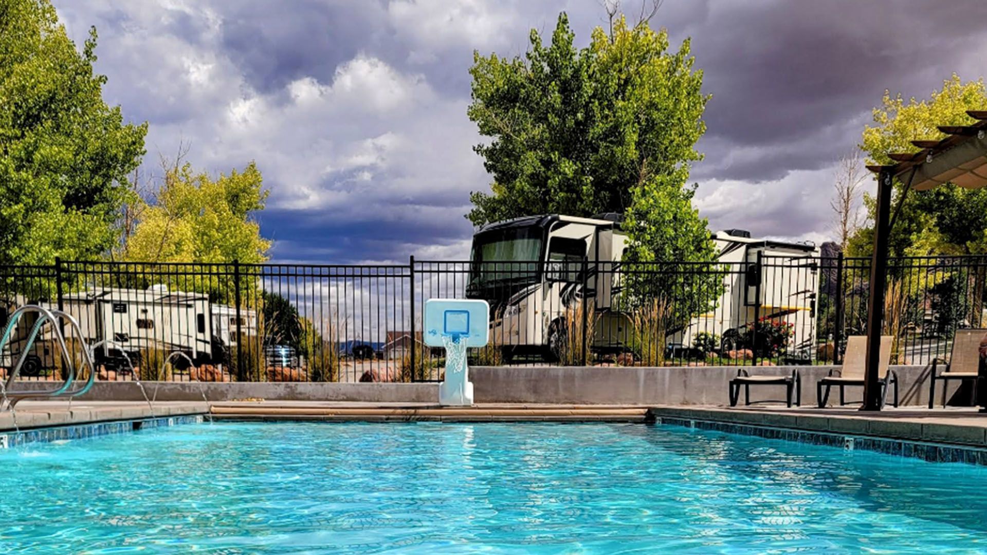 Swimming pool with a basketball hoop and RVs in the background, under a cloudy sky.